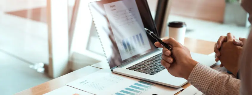 Manager is using a laptop computer while analyzing the company's financial statements on the screen.