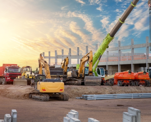 Many different multiclored colorful heavy industrial machinery equipment at construction site parking area against warehouse building city infrastructure development. Commercial vehicles rental sale